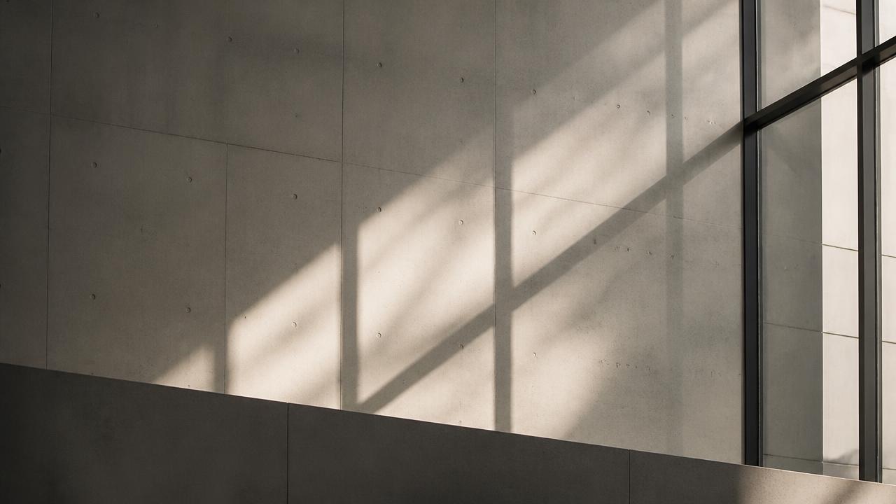 Tageslicht zeichnet ruhige Schattenlinien auf eine Betonwand hinter einer Glasfassade